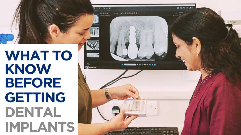 A Toftwood's dental professional shows a model of a dental implant to a smiling patient, with a dental X-ray displayed on the screen behind them.