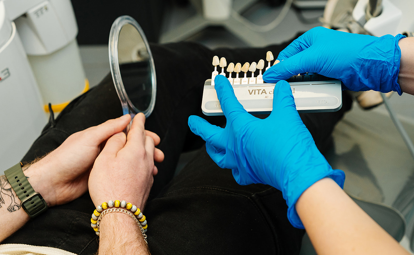 Close-up of gloved hands holding a tooth shade guide used for matching tooth color during cosmetic dental treatments like veneers.