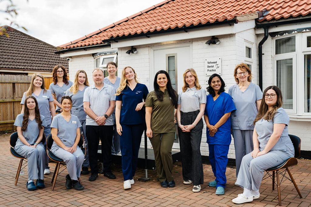 Toftwood Dental Practice team standing and sitting outside the clinic building, smiling at the camera.