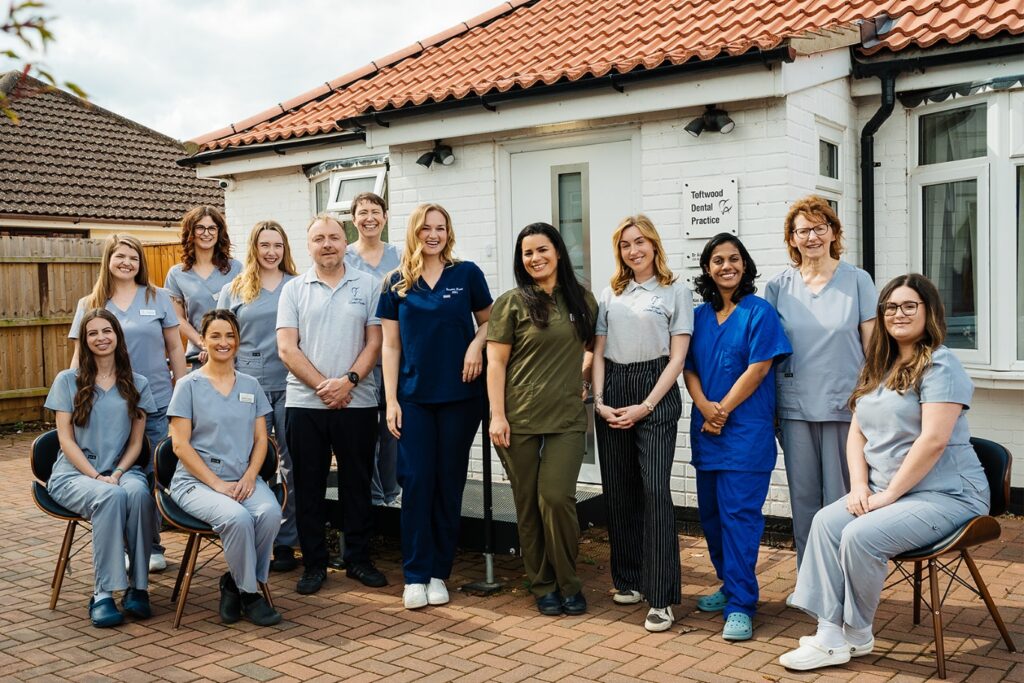Group photo of the dental team from Toftwood Dental Practice standing and sitting outside the practice building, smiling.