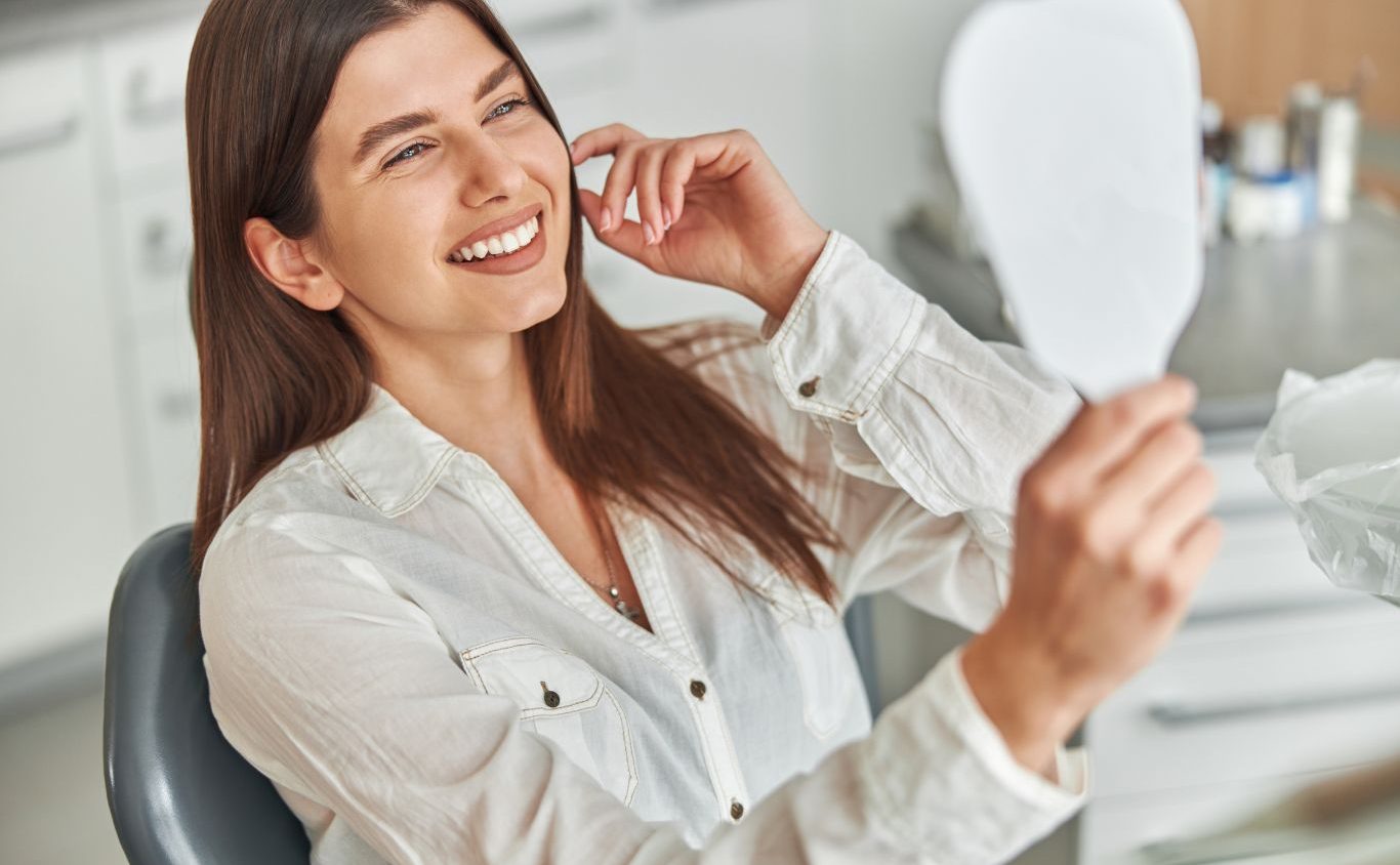 Woman at a dental practice checking her smile with a mirror